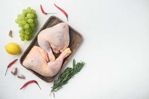 Raw meat. Chicken legs, drumsticks cuts set, with grape and parsley, on white table, top view flat lay