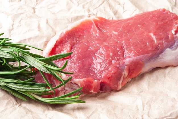 Raw meat Closeup of juicy slice of fresh raw meat with rosemary on paper