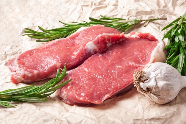 Raw meat and garlic Two pieces of fresh raw meat garlic and rosemary on paper