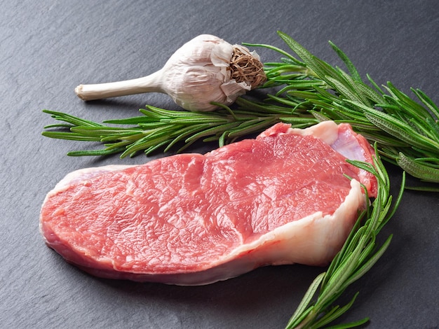 Raw meat A piece of fresh raw meat rosemary twig and garlic on black slate stone plaque