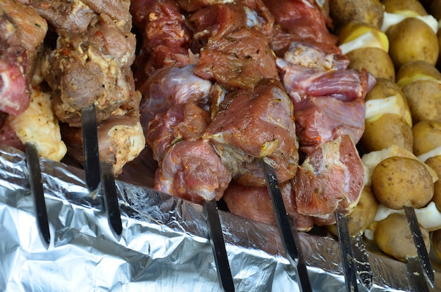 Raw meat and potatoes are planted on metal skewers. 