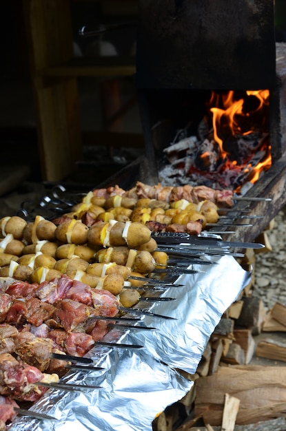 Raw meat and potatoes are planted on metal skewers.