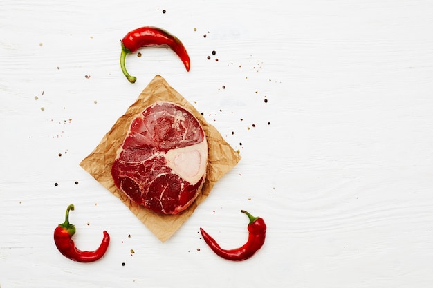 Raw meat shank with chili peppers on a white painted wooden surface