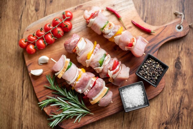 Raw meat skewers with vegetables on wooden background