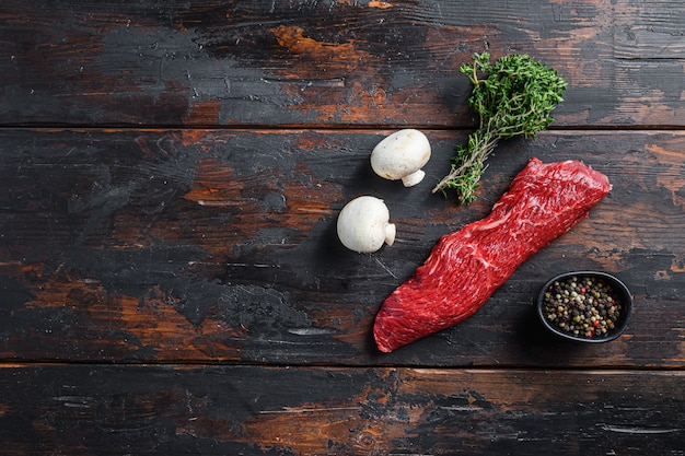 Raw meat steaks and herbs on wooden background