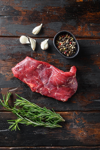 Raw meat steaks and herbs on wooden background