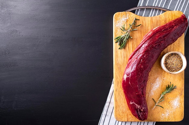 Raw meat tenderloin on wooden cutting board with spices Space for text top view