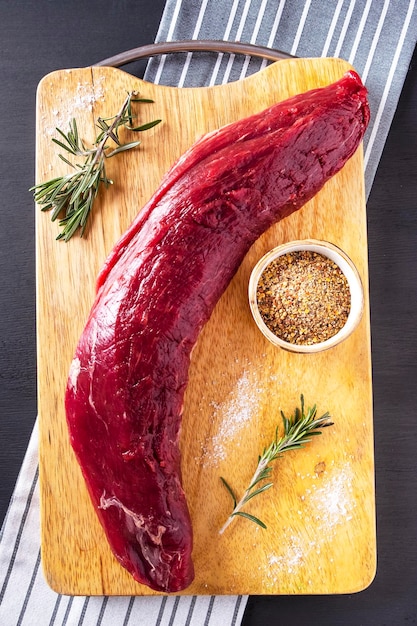 Raw meat tenderloin on wooden cutting board with spices Top view