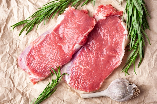 Raw meat Top view of two slices of fresh raw meat rosemary and garlic on paper