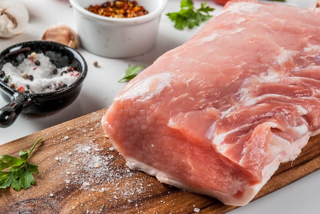 Raw meat with ingredients for dinner. Pork fillet, tenderloin, on cutting board, with salt, pepper, parsley, rosemary, oil, garlic, tomato, mushroom.Black stone table, copy space