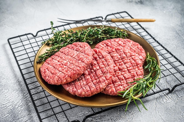 Raw minced beef burgers with spices on steel plate with rosemary and thyme White background Top view