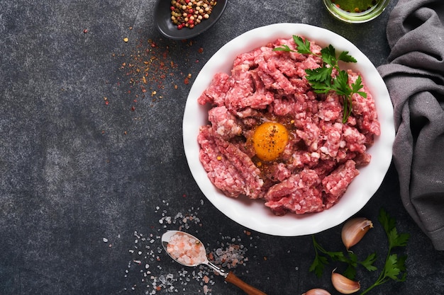 Raw minced meat Ground meat beef pork or lamb spices herbs and eggs on white plate on black old concrete background Fresh minced meat ready for cooking Food cooking background Top view