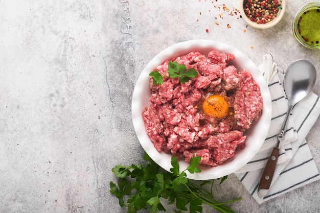 Raw minced meat Ground meat beef pork or lamb spices herbs and eggs on white plate on light grey concrete background Fresh minced meat ready for cooking Food cooking background Top view