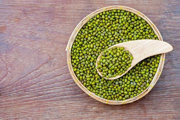 Raw mung bean in the basket and wooden spoon on wooden background, top view.