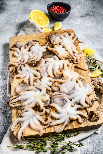 Raw octopus with thyme and lemon in a wooden bowl. Organic seafood. Gray background. Top view