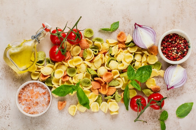 Raw orecchiette with parmesan cheese and tomatoes, basil, garlic and oil on light wall with pepper on light brown wall. Traditional ingredients for preparation of Italian pasta. Top view.