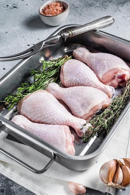 Raw organic chicken legs, drumsticks in kitchen tray with herbs. Gray background. Top view.