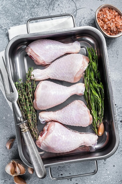 Raw organic chicken legs drumsticks in kitchen tray with herbs Gray background Top view