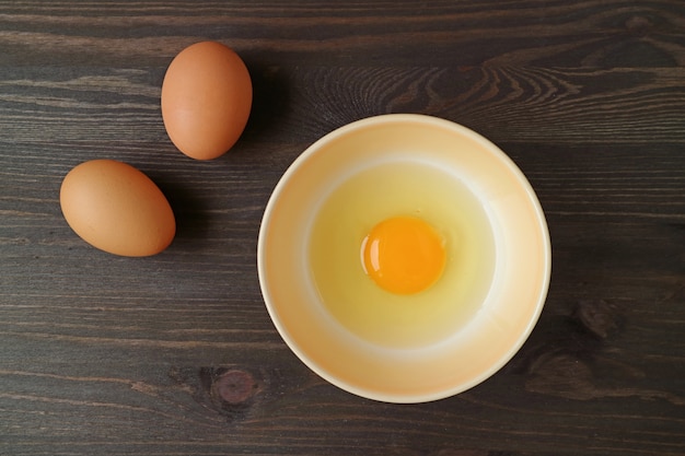 Raw organic egg in a bowl with two eggs on wooden table