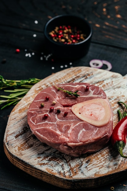 Raw Ossobuko steak marble meat with herbs and spices on dark background vertical image top view place for text