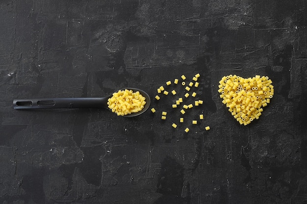 Raw pasta farfalle on wooden spoon on black background Top view of Italian cuisine ingredient