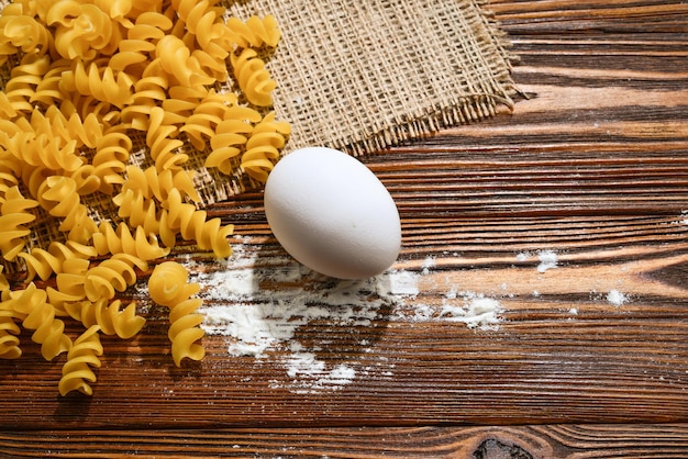 Raw pasta and ingredients for pasta on wooden background