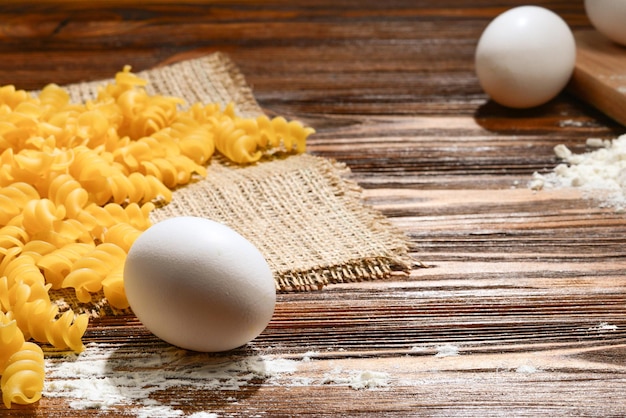 Raw pasta and ingredients for pasta on wooden background