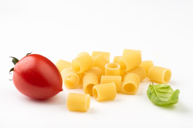 Raw pasta with basil and tomato on white surface close up