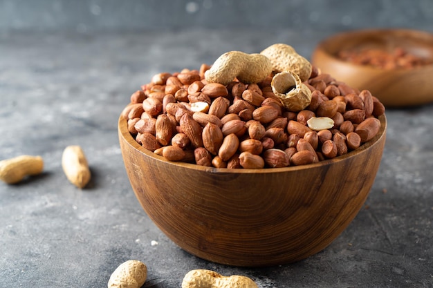 Raw peanuts in wooden bowl on natural gray rustic desk