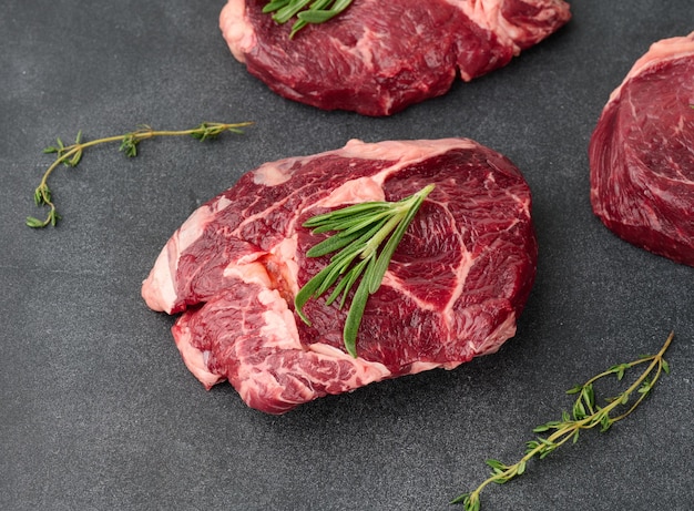 Raw piece of beef ribeye with rosemary thyme on a black table top view