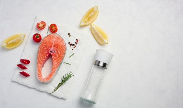 Raw piece of salmon lemon slices and spices on a white board top view