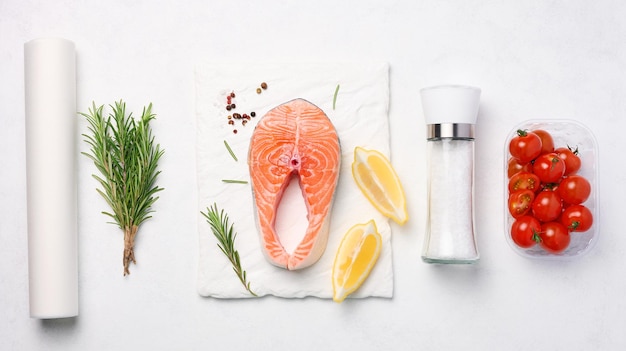 Raw piece of salmon lemon slices and spices on a white board top view