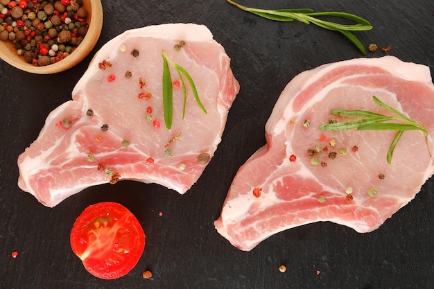 Raw pork chops on a black surface with herbs and spices