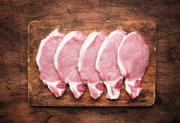 Raw pork chops meat on rustic wooden cutting board prepared for cooking with garlic thyme spices and pepper Old wood kitchen table top view