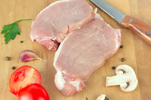 Raw pork chops of meat with garlic tomato spice pepper champignon on round cutting board with meat knife