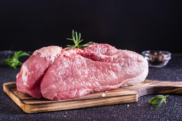 Raw pork ham salt and rosemary on a cutting board on a dark background