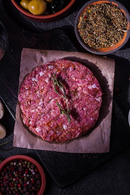 Raw pork hamburger cutlet with spices on a dark background. Home production of semi-finished products. Simple food.