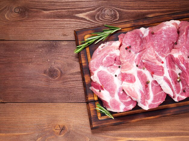 Raw Pork Loin chops on cutting board on dark wooden background, top view, copy space.