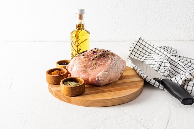 Raw pork meat on a round cutting board with bowls of different spices and rosemary oil for cooking the concept of cooking meat