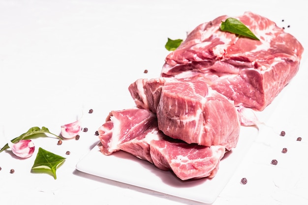 Raw pork meat, sliced cuts. Fresh meat, dry sumac, garlic and basil leaves. Healthy cooking food concept, trendy hard light, dark shadow. White putty background, copy space