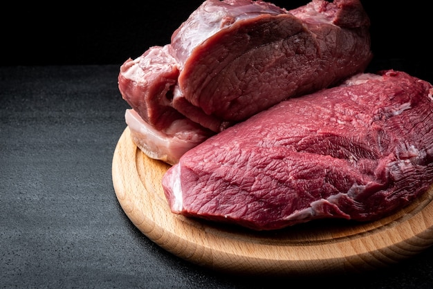 Raw pork meat on wooden board on black table.