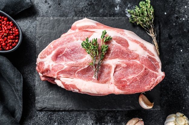 Raw pork neck chop meat with herb leaves and spices. Black background. Top view.