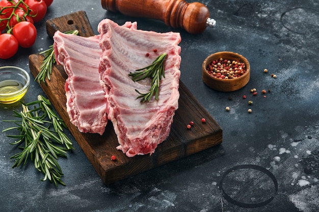 Raw pork ribs or fresh uncooked meat with spices on black wooden tray with paprika, garlic cloves and herbs. Dark textured background with copy space for text.