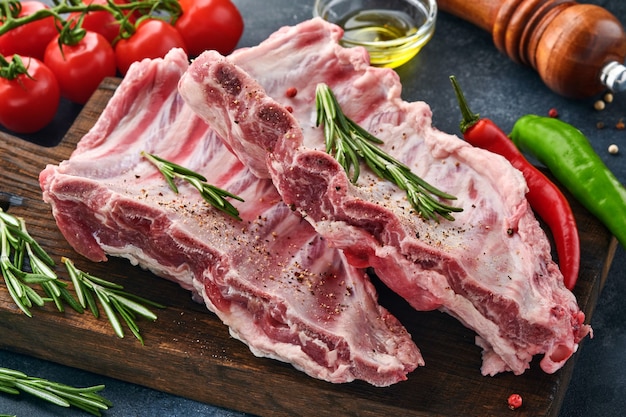 Raw pork ribs or fresh uncooked meat with spices on black wooden tray with paprika, garlic cloves and herbs. Dark textured background with copy space for text.