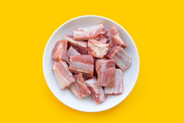 Raw pork ribs in white plate on yellow background.