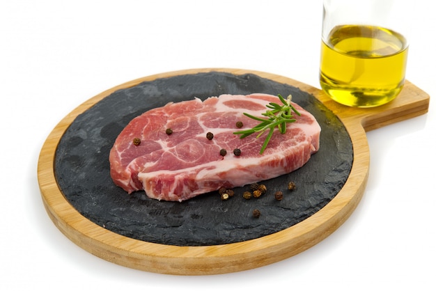 Raw pork steak on black stone with spices and oil