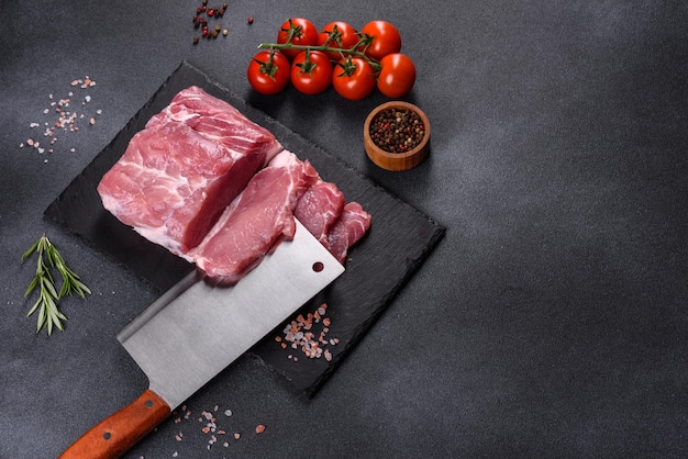 Raw pork steak on a cutting board with herbs and spices on dark stone table