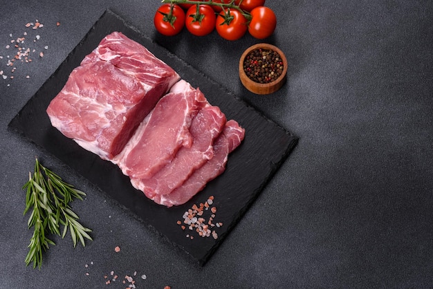 Raw pork steak on a cutting board with herbs and spices on dark stone table