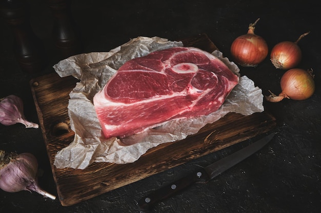 Raw pork steak on an old cutting board, knife, spices and ingredients are laid out side by side.