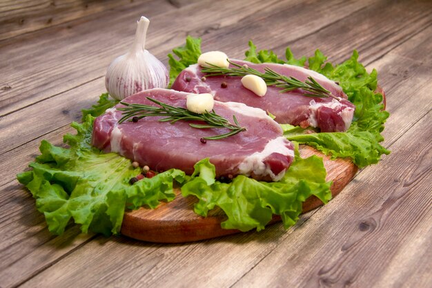 raw pork steak with green salad, rosemary, garlic and pepper on a wooden background